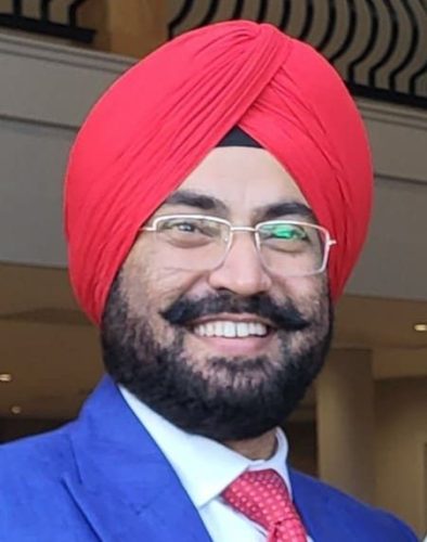 Bevan Fellow Inderpal Singh wearing a blue suit, red tie and red turban