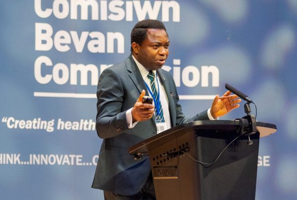 Prof Kelechi Nnoaham speaking in front of a Bevan Commission banner