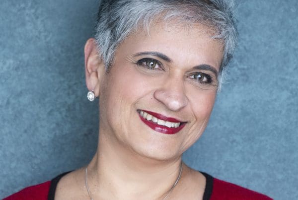 Prof Kamila Hawthorne MBE wearing a dark top and red cardigan.